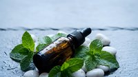 Essential oil bottle with fresh mint leaves and smooth stones on wooden surface for aromatherapy wellness spa treatment and natural healing therapy.