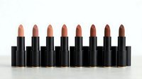 Row of eight nude and brown lipsticks in black tubes arranged on white surface. Professional cosmetics collection for makeup artists and beauty brands.