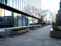 Modern urban plaza with sleek wooden benches and planters along glass office building facade, reflecting city skyline and bare winter trees on empty sidewalk.