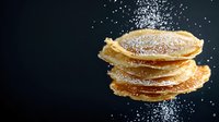 Stack of golden pancakes dusted with powdered sugar against dark background, morning breakfast food photography with dramatic lighting and copy space.