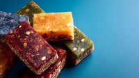 Colorful assorted energy protein bars with nuts, dried fruits and seeds on blue background. Natural healthy snacks for fitness and active lifestyle.
