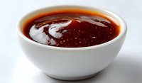 Spicy red chili sauce in white ceramic bowl on white background, close up view of Asian hot sauce with visible texture and oil separation.