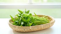 Fresh green onions and chives in woven bamboo basket on white surface, isolated against blurred background, ready for culinary use and food styling projects.