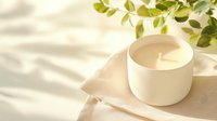 Minimalist white ceramic candle with natural leaf shadows on beige linen background, creating serene spa atmosphere for wellness and lifestyle content.