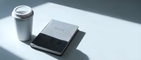 Stainless steel tumbler with lid next to closed notebook and pen on white surface, minimalist workspace setup for business and productivity content.