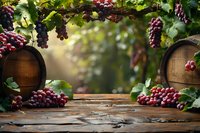 Rustic wooden table with wine barrels and fresh red grape clusters hanging from vine leaves, creating natural frame against soft blurred background for wine presentation.