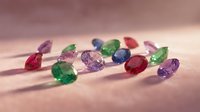 Colorful gemstones collection featuring emerald, ruby, sapphire and amethyst crystals scattered on soft pink surface for jewelry design and luxury concepts.
