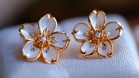 Delicate rose gold flower earrings with white enamel petals and crystal accents on soft white fabric background, elegant jewelry photography for fashion.