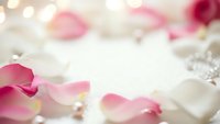 Soft pink rose petals scattered on white fabric with pearls creating romantic wedding background for invitations and feminine designs.