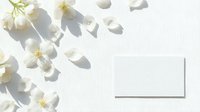 Dried white flowers and petals scattered on light background with shadows and blank card mockup for design projects.