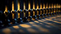 Dramatic shadows cast by ornate metal fence posts at sunset create geometric patterns. Golden light illuminates decorative wrought iron details against dark background.