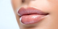 Close up of plump, glossy natural pink lips with smooth skin texture showing moisturized, healthy appearance against light background.