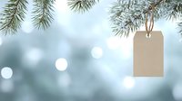 Pine branches with blank kraft paper tag hanging against soft blue bokeh winter background, festive holiday season natural decoration concept.