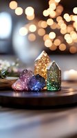 Colorful crystal houses with glitter sparkle against blurred bokeh lights background, creating magical holiday atmosphere on wooden surface with decorative elements.