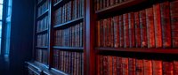 Vintage library interior with wooden bookshelves filled with antique leather-bound books in warm lighting for academic and literary projects.