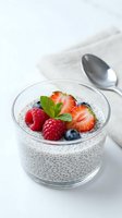 Chia seed pudding topped with fresh berries and mint in glass bowl on white marble surface for healthy breakfast or dessert recipes.