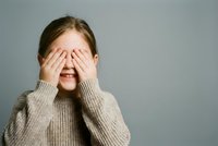 Young Caucasian woman covering eyes with hands wearing beige knit sweater expressing surprise shame or playing peek-a-boo game on neutral background.