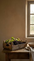 Dark grapes in rustic wooden crate on aged table by window with natural light, suitable for food styling, culinary content, and harvest themes.