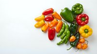 Assorted fresh bell peppers in red, yellow, orange, and green varieties arranged on white background for culinary and healthy eating content.
