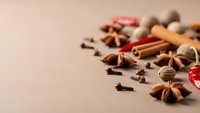 Aromatic spices scattered on beige background including cinnamon sticks, star anise, cloves, cardamom and chili peppers for cooking and baking recipes.