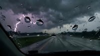 Rainy day driving view through windshield with water droplets on glass, stormy weather conditions on empty road ahead creating moody atmospheric scene.