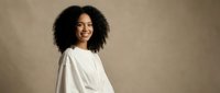 Happy young African American woman with curly hair smiling in white casual top against neutral beige background for lifestyle and portrait photography.