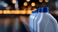 White plastic motor oil containers with blue caps on blurred bokeh background with warm golden lights, automotive maintenance concept.