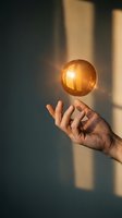Hand holding glowing golden sphere against sunlit wall with shadows, representing innovation, ideas, energy, success, and business concepts for corporate and creative projects.