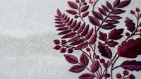Burgundy botanical embroidery on white linen fabric featuring delicate fern leaves and foliage in rich wine red thread creating elegant textile art.