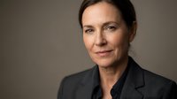 Middle-aged woman with dark hair wearing black blazer against neutral gray background, professional headshot for corporate, business, and executive portraits.