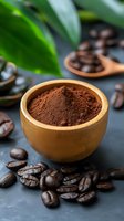 Ground coffee powder in wooden bowl with roasted beans and green leaves on dark slate surface for brewing and cafe menu design.
