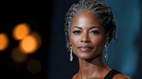 Elegant African American woman with braided updo hairstyle and crystal earrings smiling confidently against dark background with soft bokeh lights.