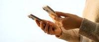 Man with medium skin tone holding two smartphones, wearing a beige sweater, isolated on white background for app design, technology marketing, and digital communication projects.
