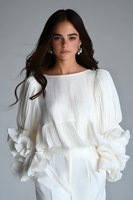 Young Hispanic woman in elegant white ruffled blouse with dramatic puff sleeves and layered details against gray background, fashion portrait with flowing dark hair.