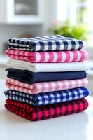 Stack of colorful folded kitchen towels with gingham and checkered patterns on white counter in bright modern home interior for cooking and cleaning.