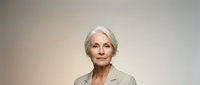 Mature woman with white hair wearing beige blazer against neutral background, suitable for corporate, business, and professional portraits.