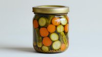 Mixed pickled vegetables in glass mason jar with carrots, cucumbers and spices on white background, homemade preservation for healthy eating and food storage.