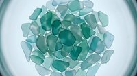 Polished sea glass fragments in shades of green and blue arranged on white surface, suitable for design, craft projects, and decorative backgrounds.