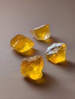 Raw amber stones with natural translucent glow on neutral background, glowing yellow crystals with rough surface texture and light reflection.