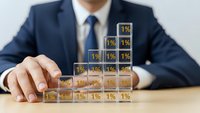 Professional businessman in navy suit building percentage blocks showing growth from 1% to 10%, representing business development and financial progress concept.