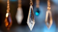 Crystal prism pendant hanging with bokeh lights in background creating elegant luxury jewelry display for home decor and spiritual wellness concepts.
