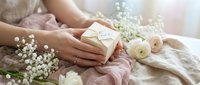 Woman hands holding wrapped gift box with flowers and soft fabric creating romantic present giving scene for special occasions and celebrations.