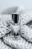 Elegant crystal perfume bottle with silver cap on textured white surface. Luxury fragrance container with geometric cut glass design creates sophisticated mood.