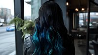 Young woman with long wavy black hair featuring vibrant turquoise blue ombre highlights, wearing leather jacket, photographed from behind in urban cafe setting.