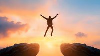 Silhouette of person jumping between mountain cliffs at dramatic sunset with orange and blue sky, symbolizing success, achievement and overcoming challenges.
