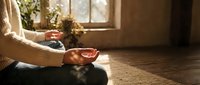 Woman practicing meditation in cozy home interior with warm sunlight streaming through window creating peaceful mindful moment for wellness and relaxation.