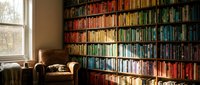 Cozy home library with rainbow organized bookshelf wall and comfortable leather reading chair by window. Literary sanctuary for book lovers and readers.