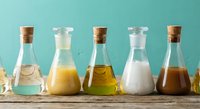 Glass bottles with cork stoppers containing colorful liquids and powders arranged on wooden surface for laboratory or kitchen experiments.