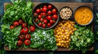 Fresh Mediterranean ingredients on rustic wooden board with cherry tomatoes, chickpeas, herbs, feta cheese and orange dressing for healthy salad preparation.