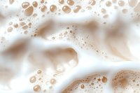 Creamy coffee foam macro with bubbles and swirls in light beige and white tones creates abstract background pattern for cafe and beverage designs.